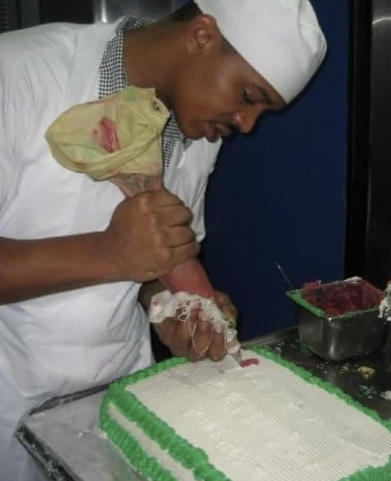 Geoff Cole in a white chef coat and hat, piping frosting onto a sheet cake at a bakery station