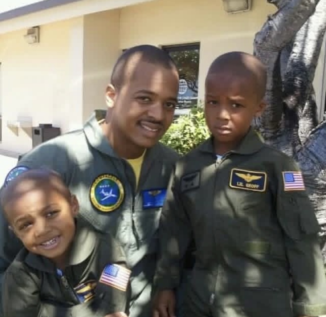 A man and two boys in olive flight suits covered with patches, posing together outdoors
