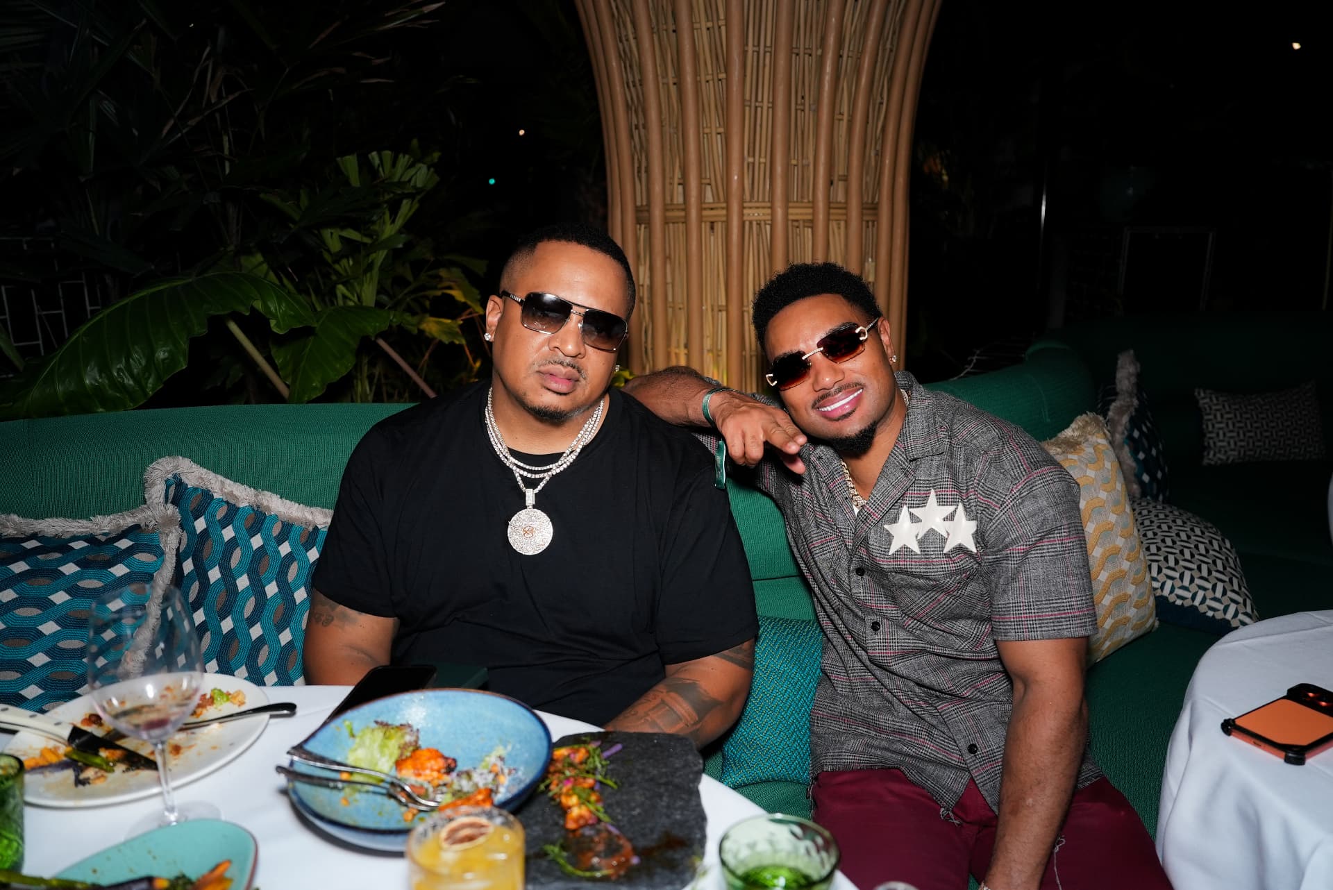 Geoff Cole in sunglasses seated at a restaurant table with another man, dinner plates in front of them